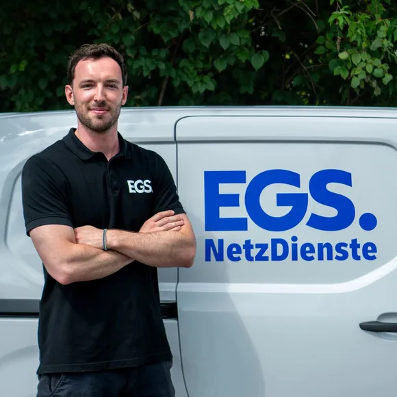 EGS-Monteur in Arbeitskleidung, mit verschränkten Armen vor einem weißen EGS-Einsatzfahrzeug